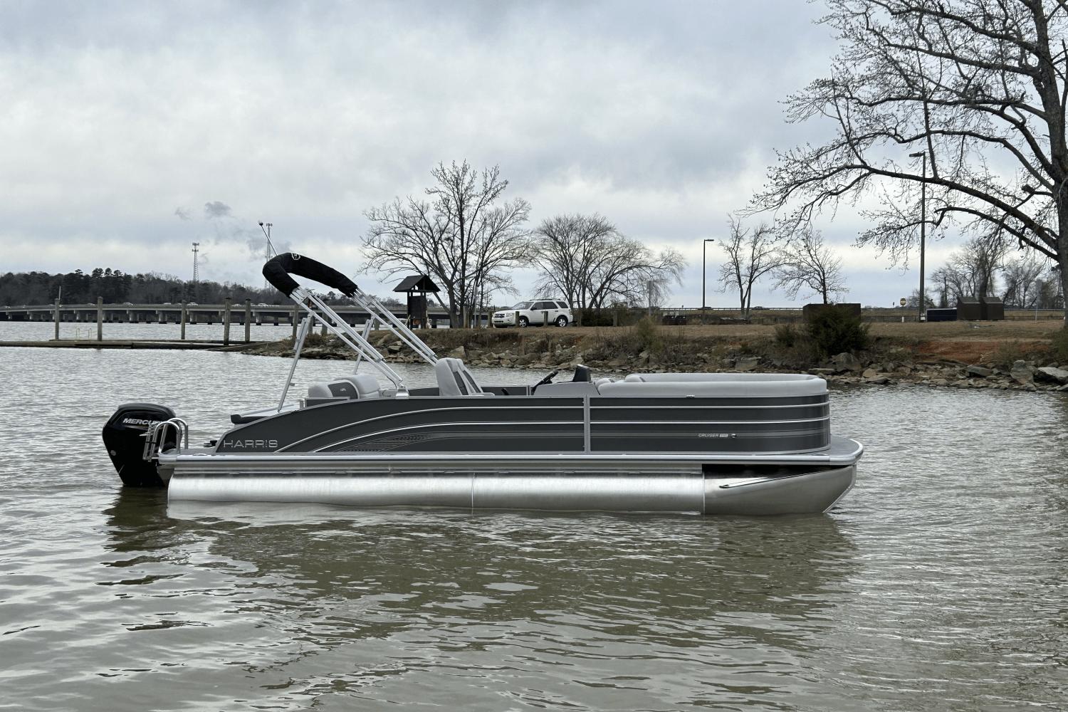 Harris Cruiser 230 2024 Harris Cruiser 230 pontoon boat on a lake with a cloudy sky.