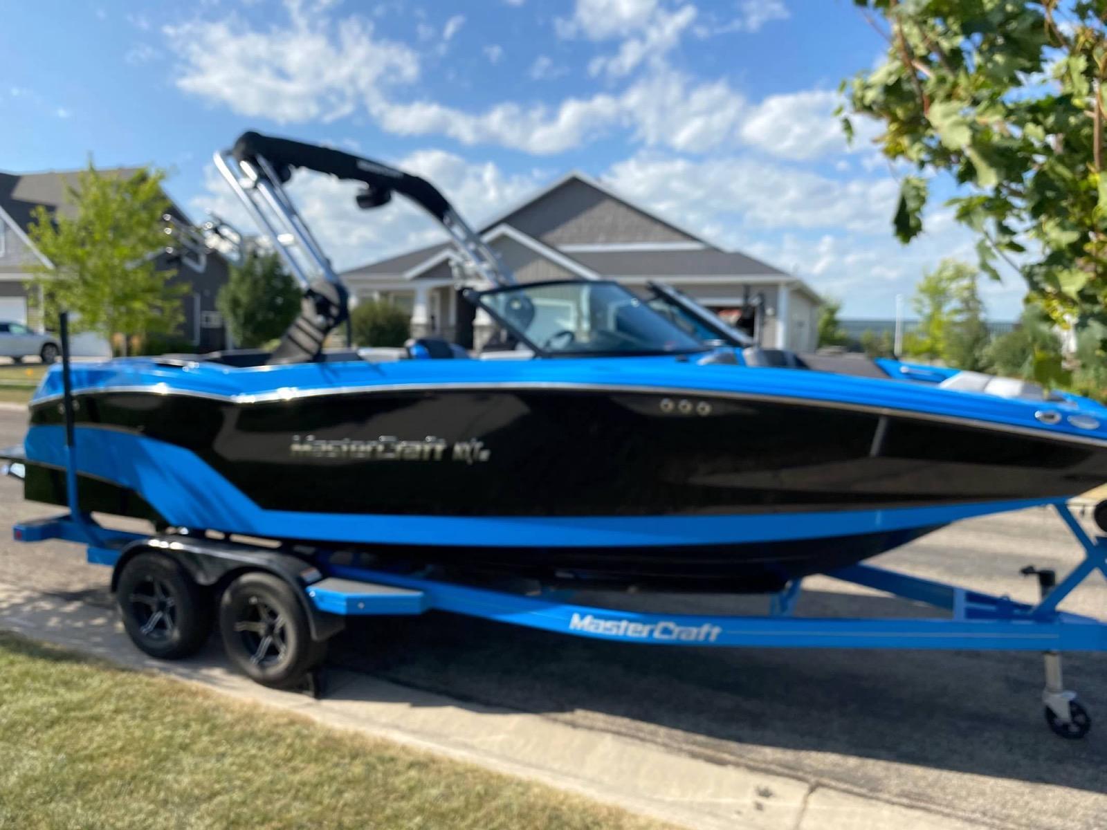 MasterCraft NXT22 2020 MasterCraft NXT22 boat in blue and black on a trailer, parked in a suburban area.