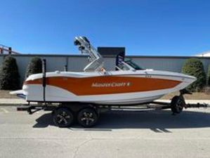 MasterCraft X22 2024 MasterCraft X22 boat on trailer, orange and white design, parked outdoors.