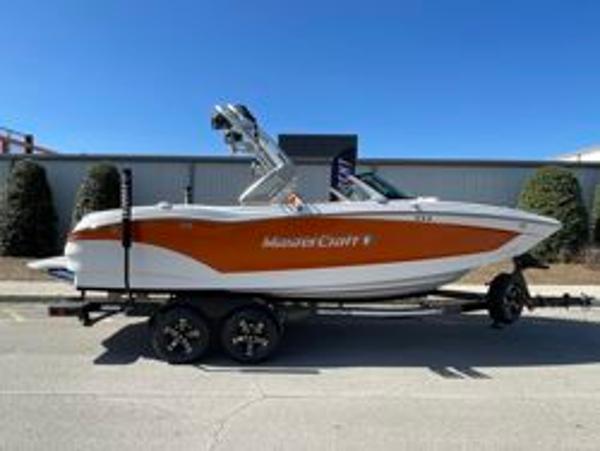 MasterCraft X22 2024 MasterCraft X22 boat on trailer, orange and white design, parked outdoors.