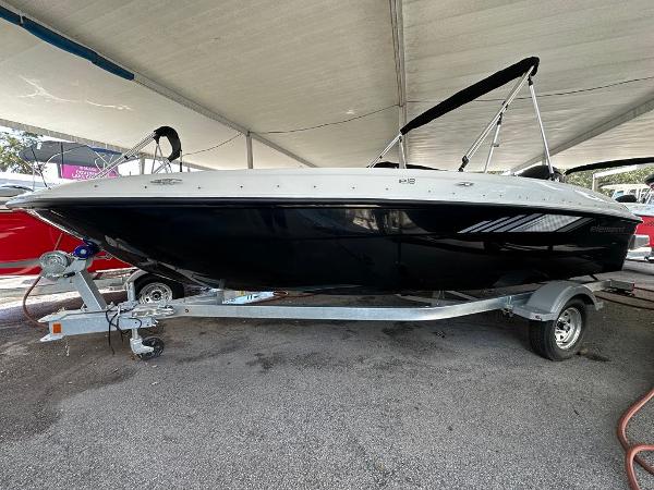 Bayliner E18 2025 Bayliner E18 boat on trailer under canopy, side view.