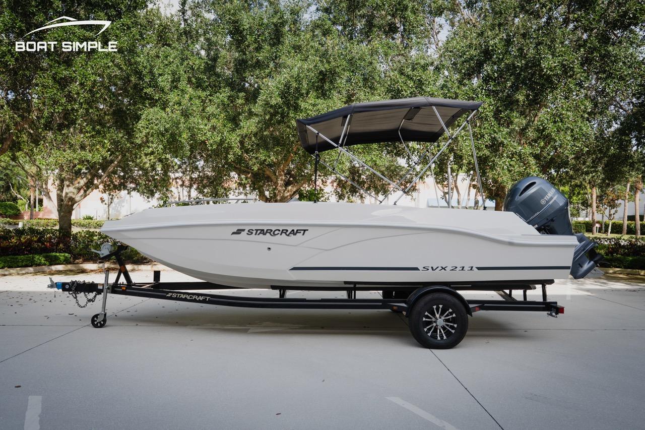 Starcraft SVX 211 OB 2023 Starcraft SVX 211 OB boat on trailer, parked outdoors with trees in background.