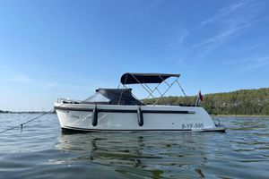 Maxima 620 2022 Maxima 620 boat on calm water, clear sky, forested shoreline.
