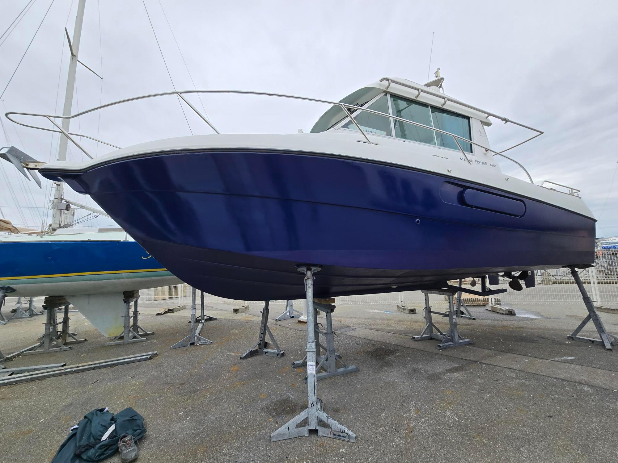 Jeanneau MERRY FISHER 800 1993 Jeanneau MERRY FISHER 800 boat on stands, blue hull, docked outdoors.