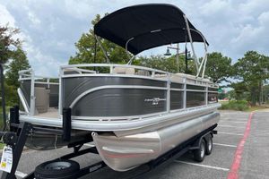 Sun Tracker Fishin' Barge 20 DLX 2025 Sun Tracker Fishin' Barge 20 DLX pontoon boat on trailer in parking lot.