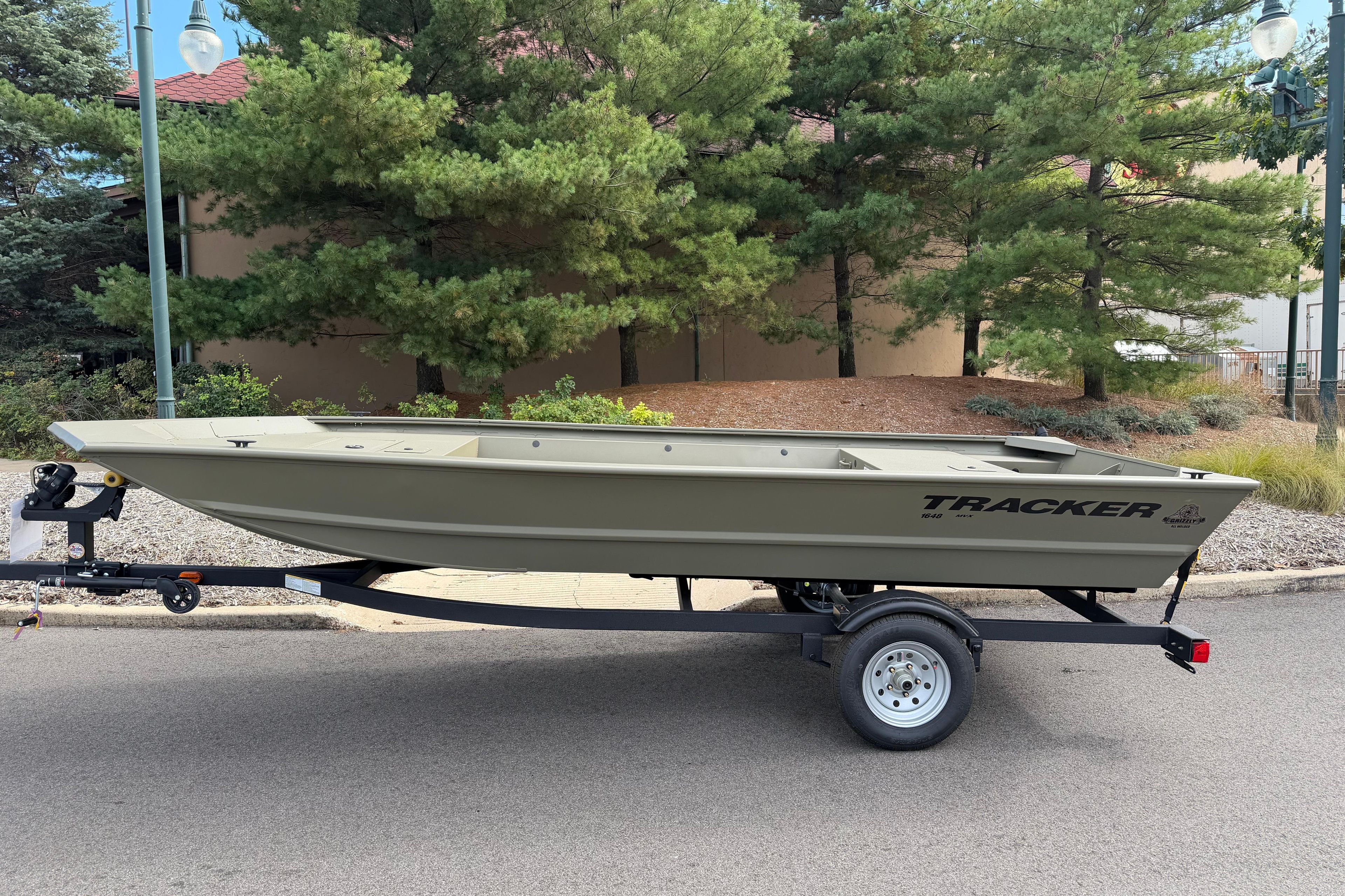 Tracker Grizzly 1648 Utility 2026 Tracker Grizzly 1648 Utility boat on trailer, parked near trees.