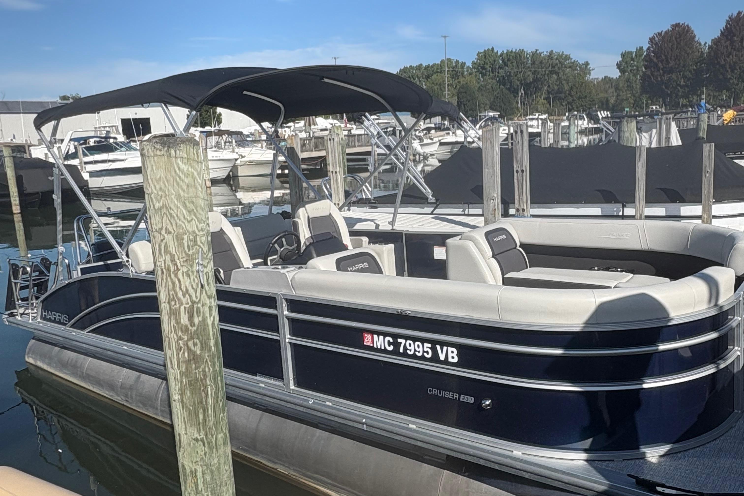 Harris Cruiser 230 2025 Harris Cruiser 230 pontoon boat docked at a marina under a clear blue sky.