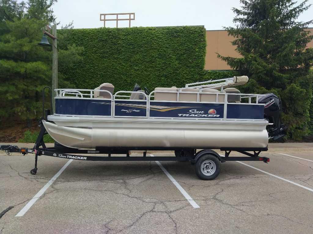 Sun Tracker Bass Buggy 18 DLX 2025 Sun Tracker Bass Buggy 18 DLX pontoon boat on trailer in parking lot.