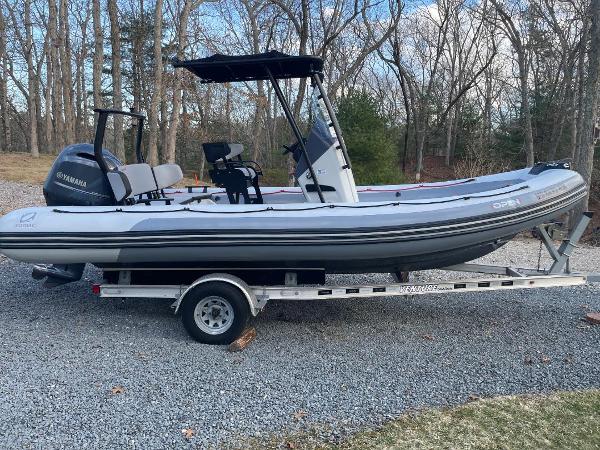 Zodiac Open 6.5 2020 Zodiac Open 6.5 boat on trailer, parked on gravel, surrounded by trees.