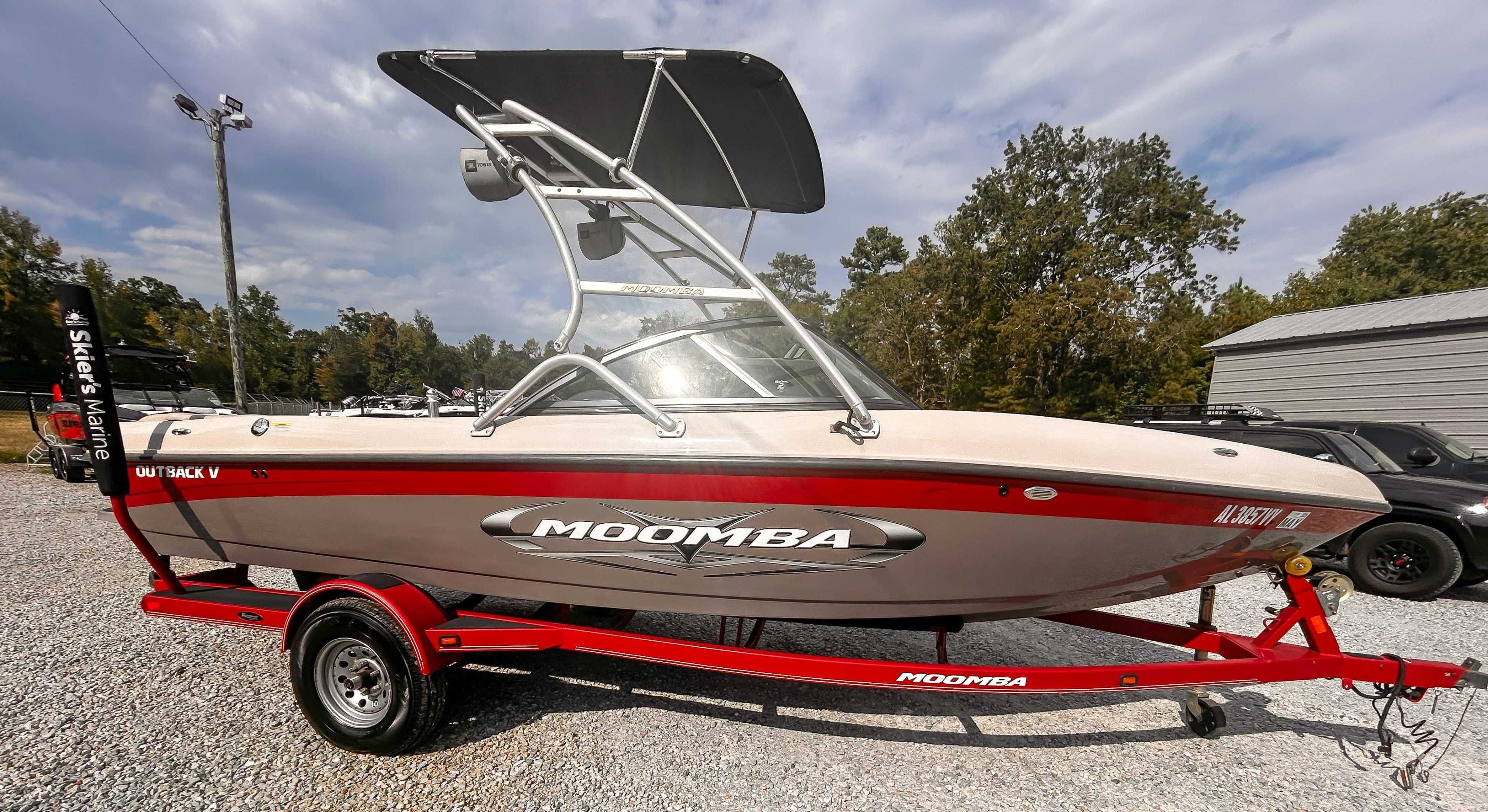 Moomba Outback V 2010 Moomba Outback V boat on red trailer, parked outdoors on gravel.