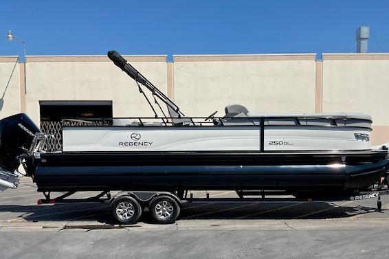 Regency 250 DL3 2025 Regency 250 DL3 pontoon boat on trailer, parked outdoors, side view.