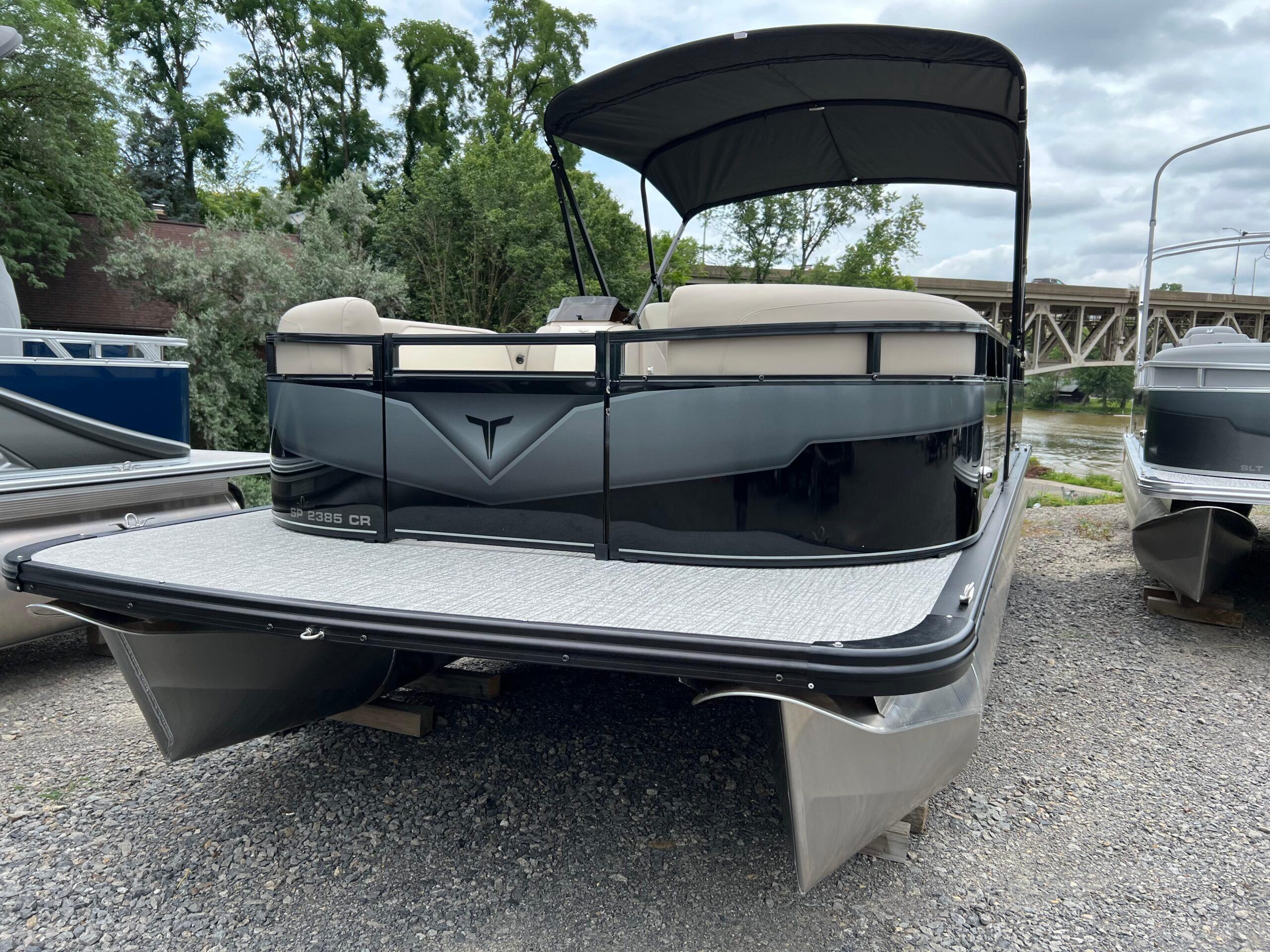 Tahoe Pontoon SPORT 85 2385 CRUISE 2026 Tahoe Pontoon SPORT 85 2385 CRUISE on gravel near river and trees.