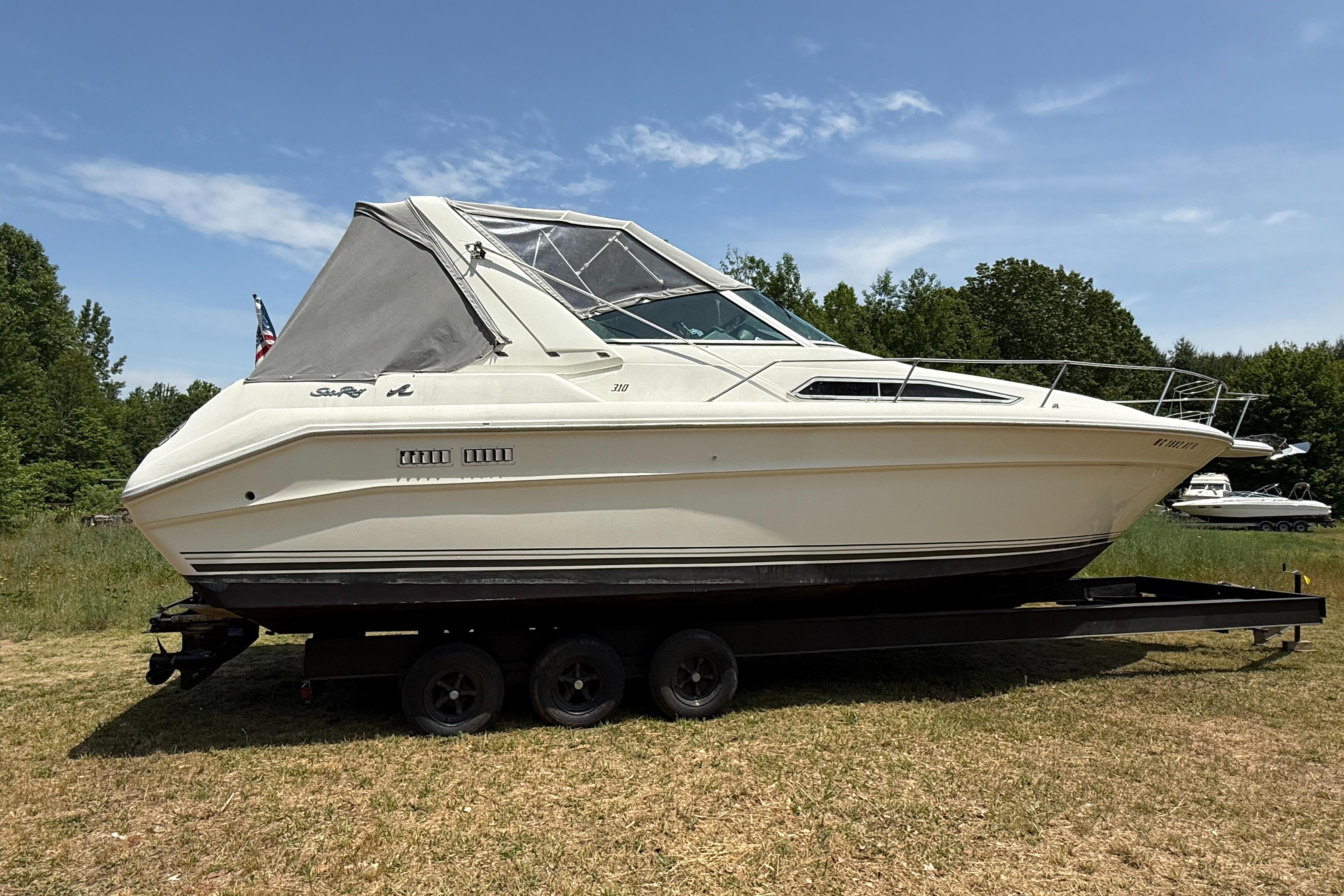 Sea Ray 310 Sundancer 1990 Sea Ray 310 Sundancer boat on trailer, parked on grass under clear sky.
