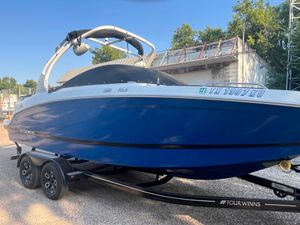 Four Winns HD3 Surf 2023 Four Winns HD3 Surf boat on trailer, blue and white design, parked outdoors.