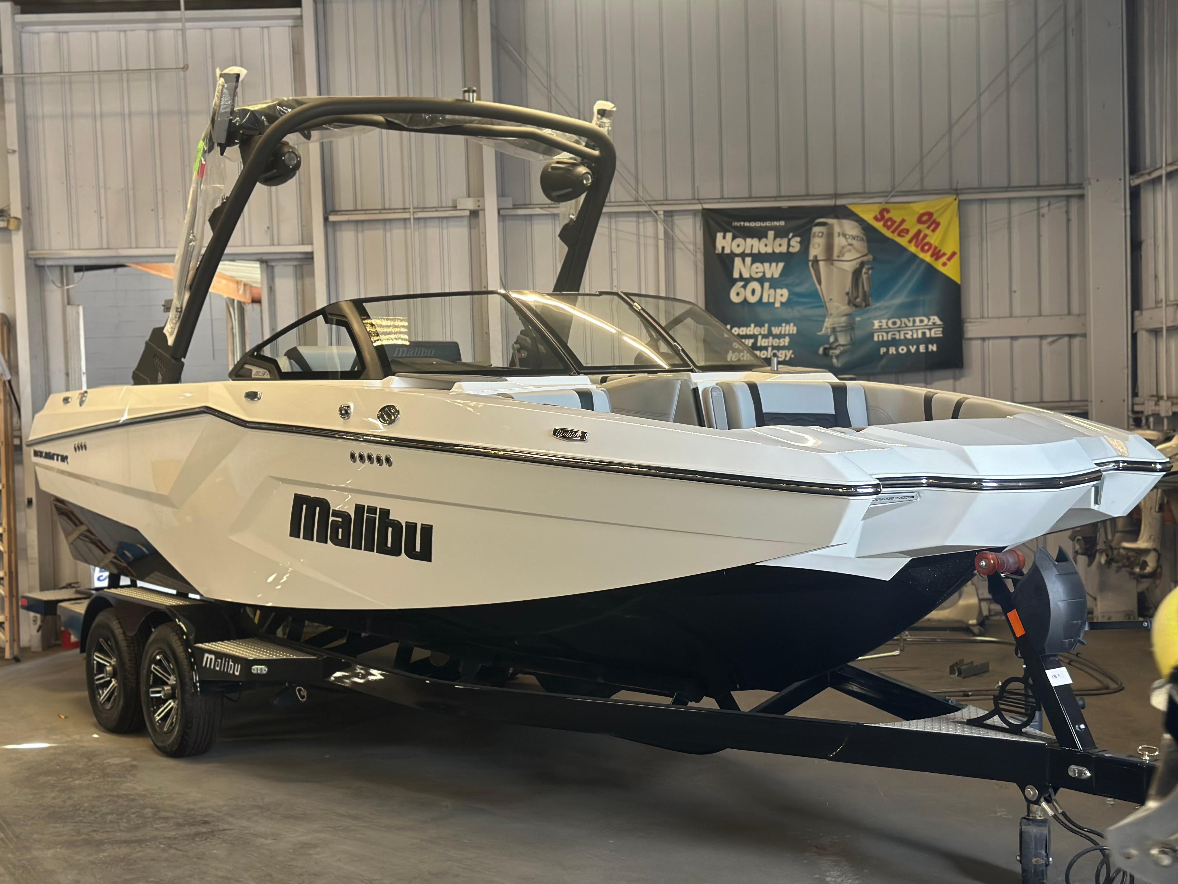 Malibu Wakesetter 23 MXZ 2025 Malibu 23 MXZ boat in showroom, sleek design, white exterior, on trailer.