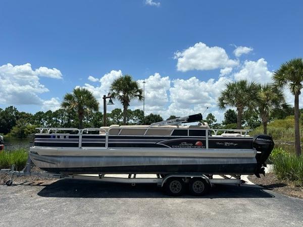 Sun Tracker fishing barge 24 2015 Sun Tracker Fishing Barge 24 pontoon boat on trailer, parked near palm trees.