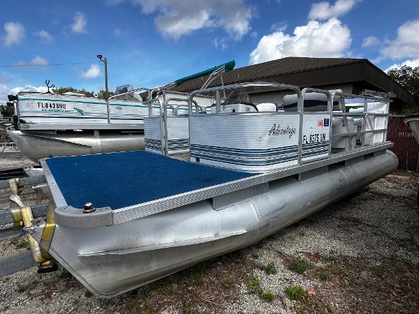 Sylvan Adventure 1994 Sylvan Adventure pontoon boat with blue deck, parked outdoors under a cloudy sky.