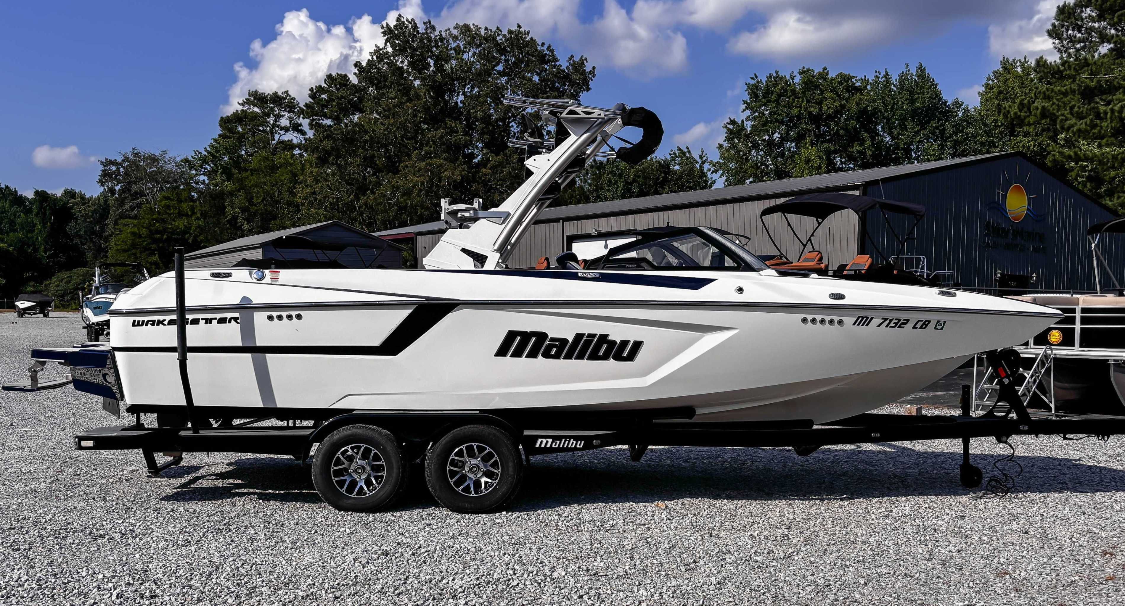 Malibu Wakesetter 24 MXZ 2021 Malibu Wakesetter 24 MXZ boat on trailer, parked outdoors under blue sky.
