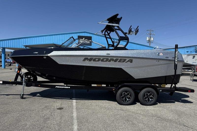 Moomba Max 2026 Moomba Max boat on trailer in parking lot, blue building background.