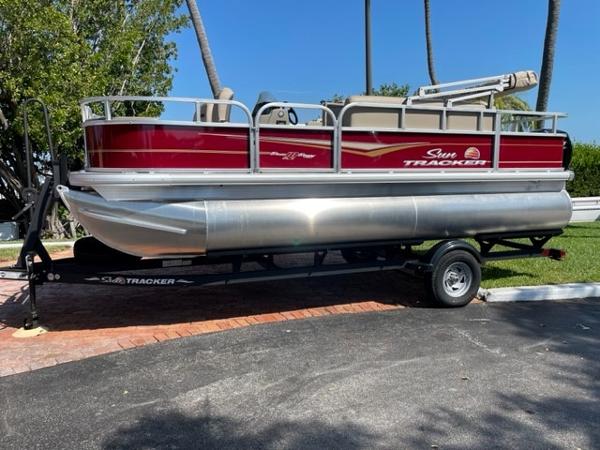 Sun Tracker Bass Buggy 18 DLX 2024 Sun Tracker Bass Buggy 18 DLX pontoon boat on a trailer, parked outdoors.