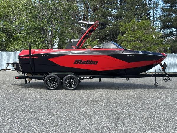 Malibu Wakesetter Lsv 23 2025 Malibu 23 LSV boat in red and black on a trailer, parked outdoors.
