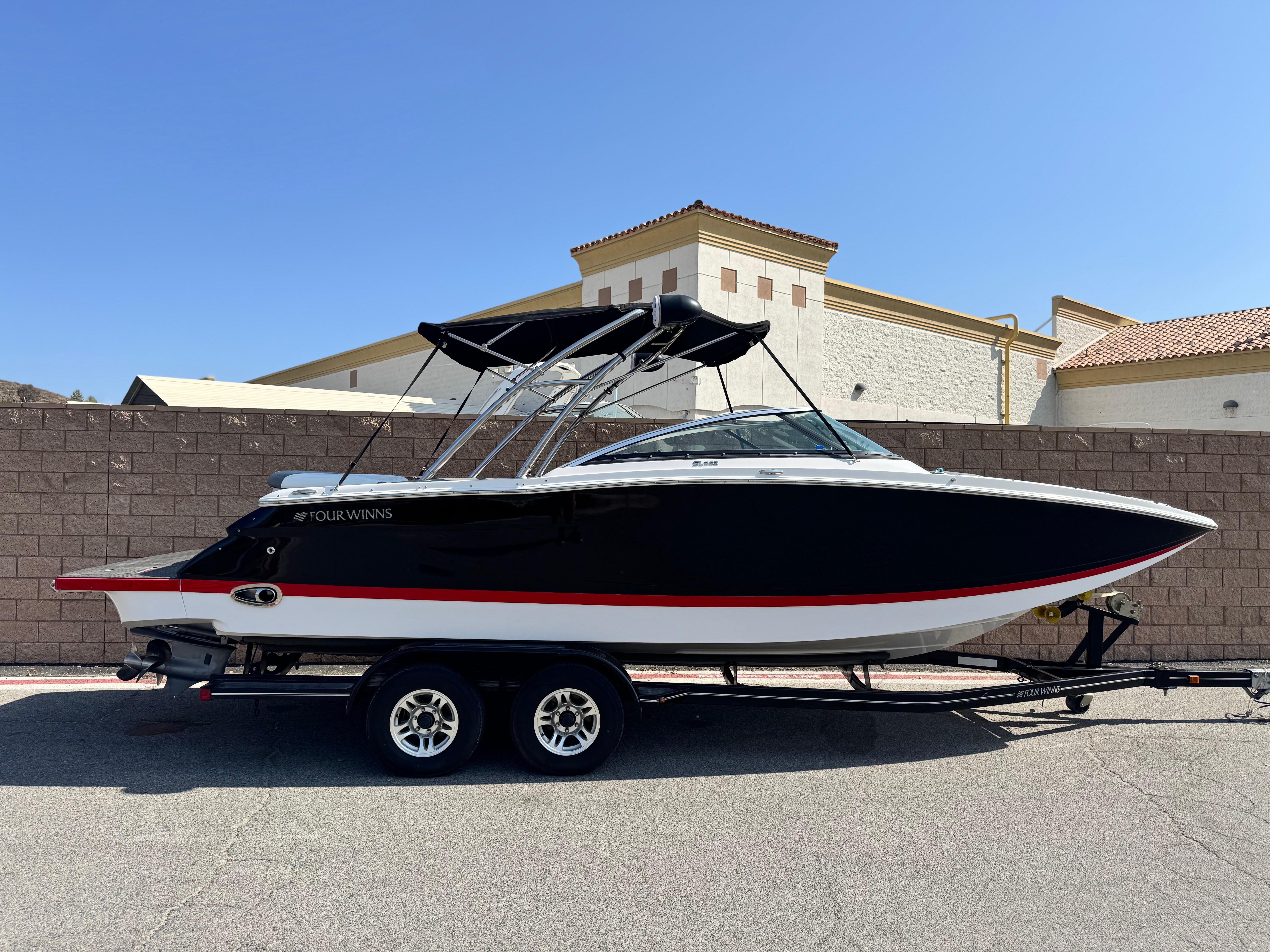 Four Winns SL262 2008 Four Winns SL262 boat on trailer, black and white with red stripe, parked outdoors.