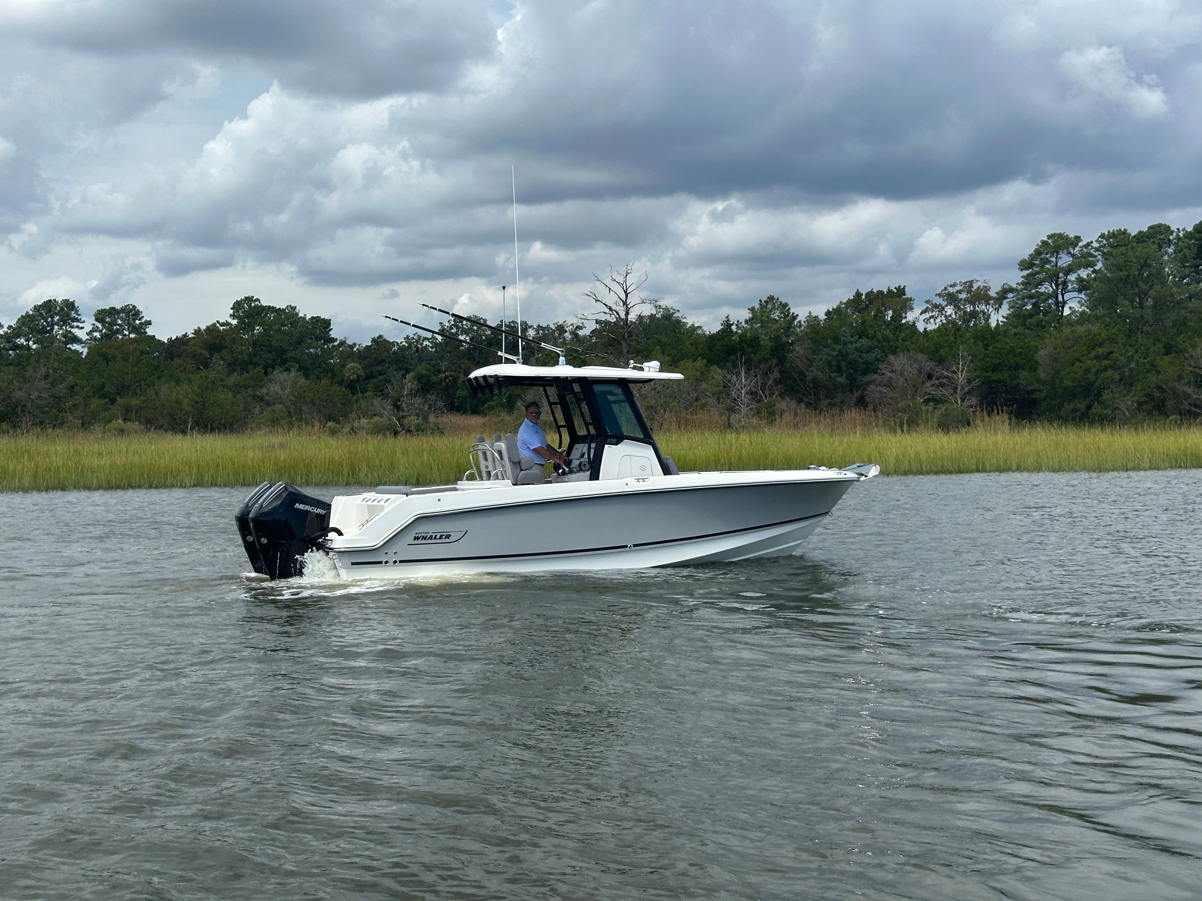 Boston Whaler 250 Outrage 2025 Boston Whaler 250 Outrage boat cruising on a calm river under cloudy skies.