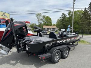Tracker Savage 215 2025 Tracker SAVAGE™ 215 boat on trailer, parked outdoors near trees and buildings.