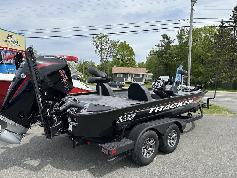 Tracker Savage 215 2025 Tracker SAVAGE™ 215 boat on trailer, parked outdoors near trees and buildings.