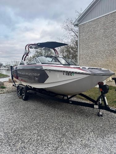 Nautique Super Air G23 2013 Nautique Super Air G23 boat on trailer, parked on gravel near a brick building.