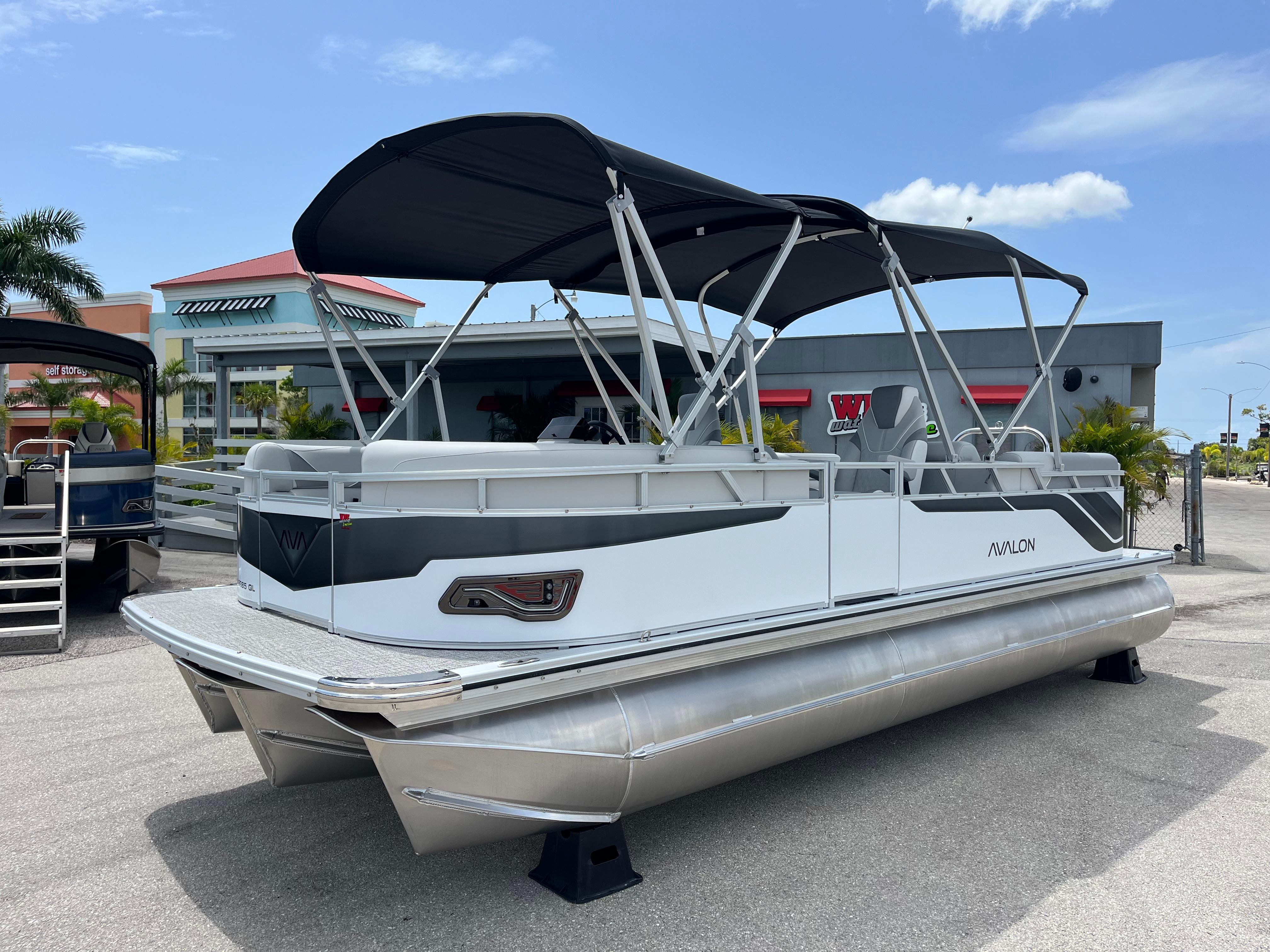 Avalon 2385 Venture 85 Quad Lounger, Tri Toon High Performance 2025 Avalon 2385 Venture 85 Quad Lounger Tri Toon boat with canopy, parked outdoors.