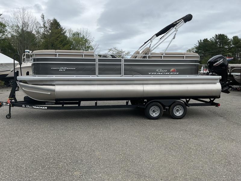 Sun Tracker Party Barge 22 DLX 2025 Sun Tracker PARTY BARGE® 22 DLX pontoon boat on trailer, parked outdoors.