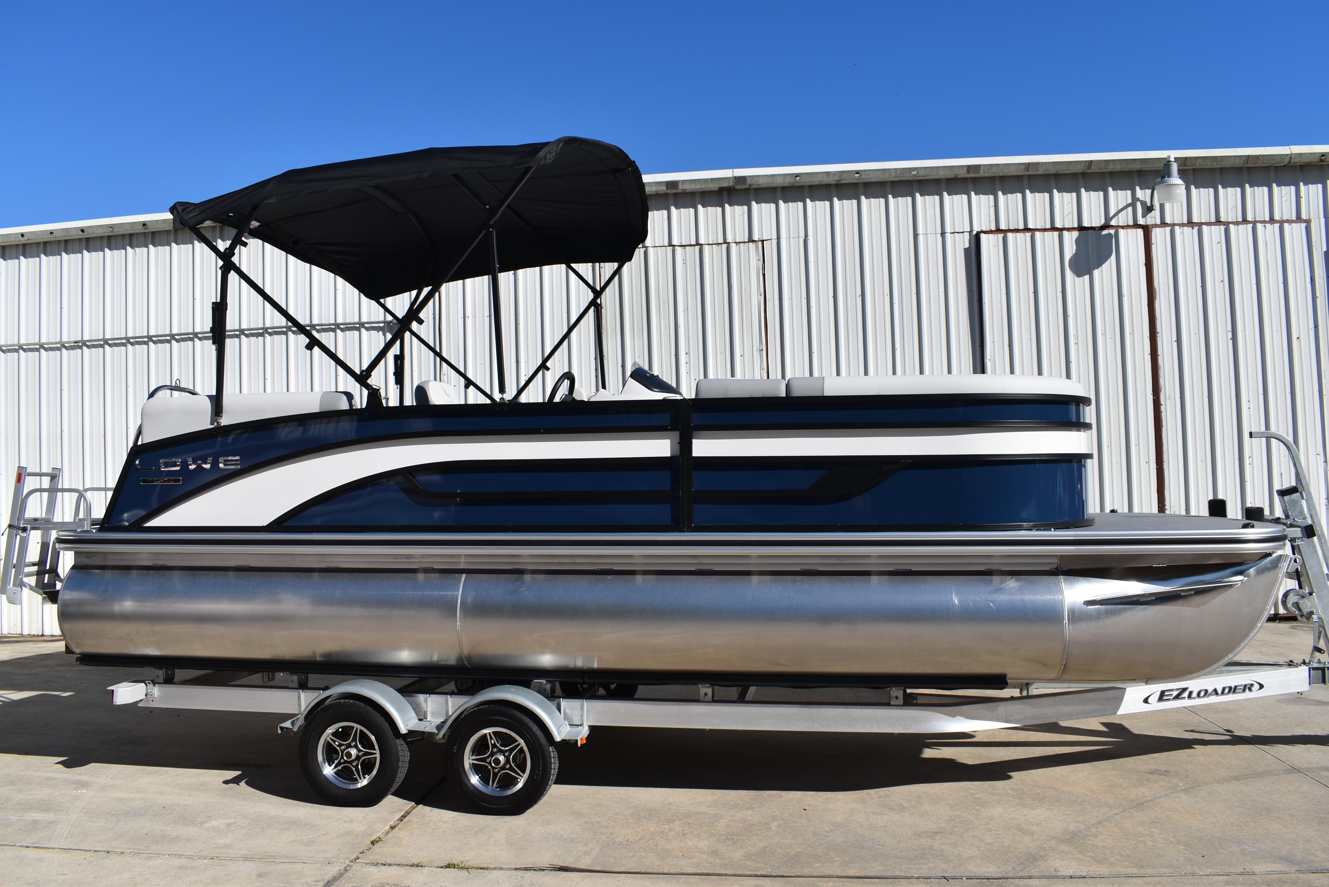 Lowe SS 230 WV TL 2025 Lowe SS 230 WV pontoon boat on trailer, parked by a metal building.