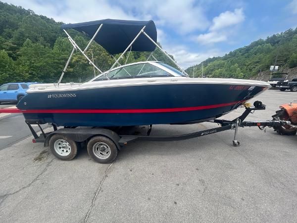 Four Winns H210 2017 Four Winns H210 boat on trailer, blue hull, parked outdoors with trees in background.