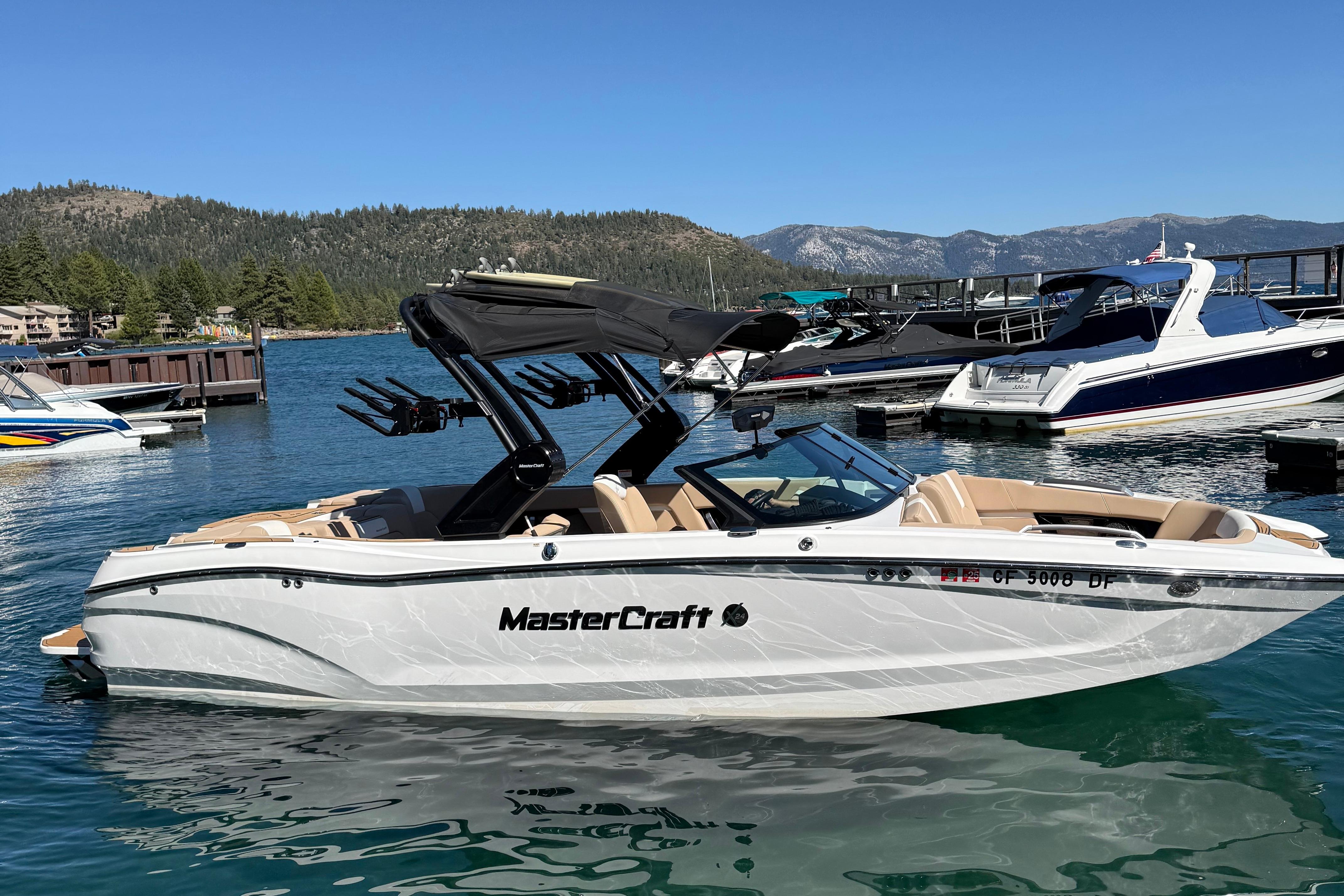 MasterCraft X24 2025 MasterCraft X24 boat docked on a serene lake with mountain backdrop.