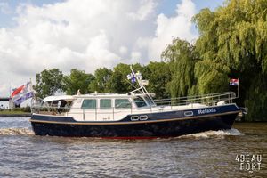 Kuster A-38 Kuster A-38 boat from 2004 cruising on a river, surrounded by lush greenery.