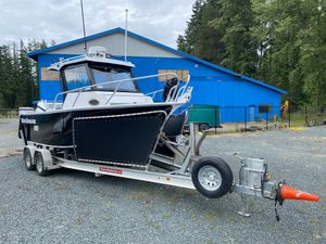 Custom 625 Custom 2023 model 625 boat on trailer, parked near blue building, surrounded by trees.