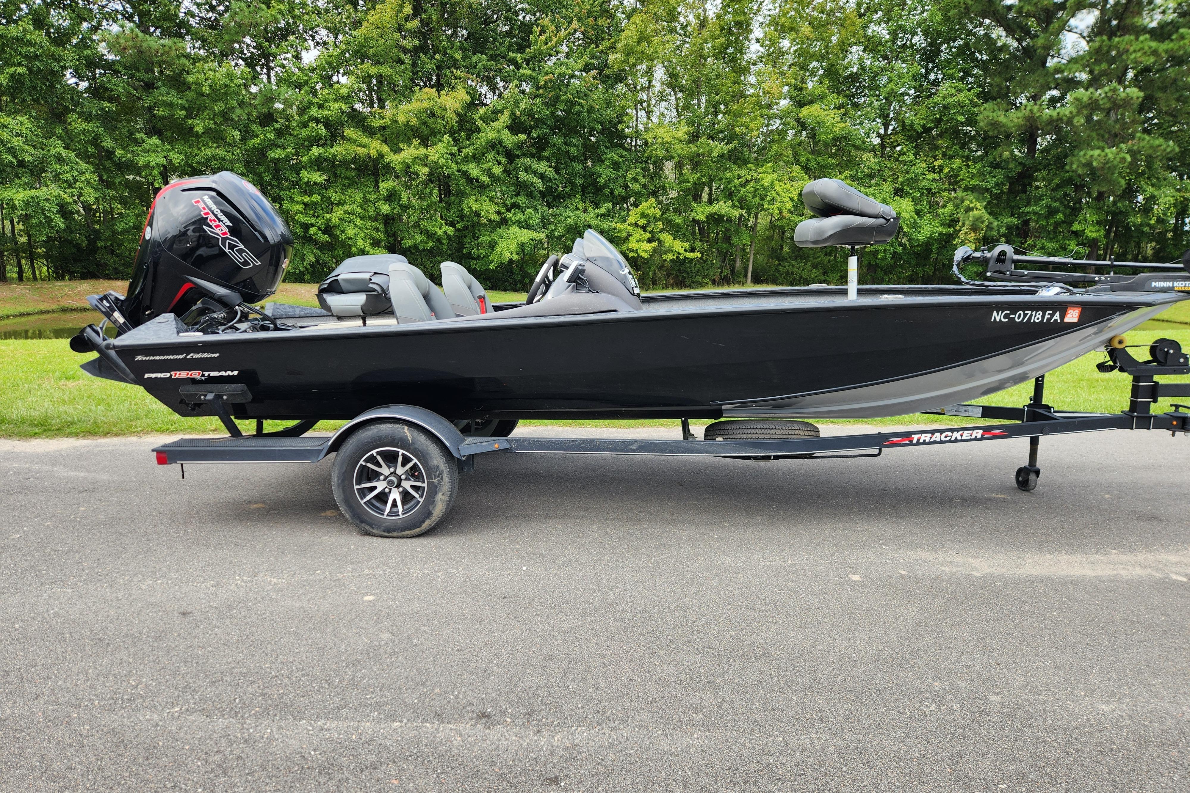 Tracker Pro Team 190 TX 2023 Tracker Pro Team 190 TX boat on trailer, parked on road with green trees background.