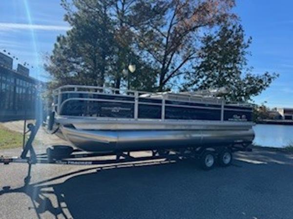Sun Tracker Fishin' Barge 22 DLX 2025 Sun Tracker Fishin' Barge 22 DLX pontoon boat on trailer by a lake.