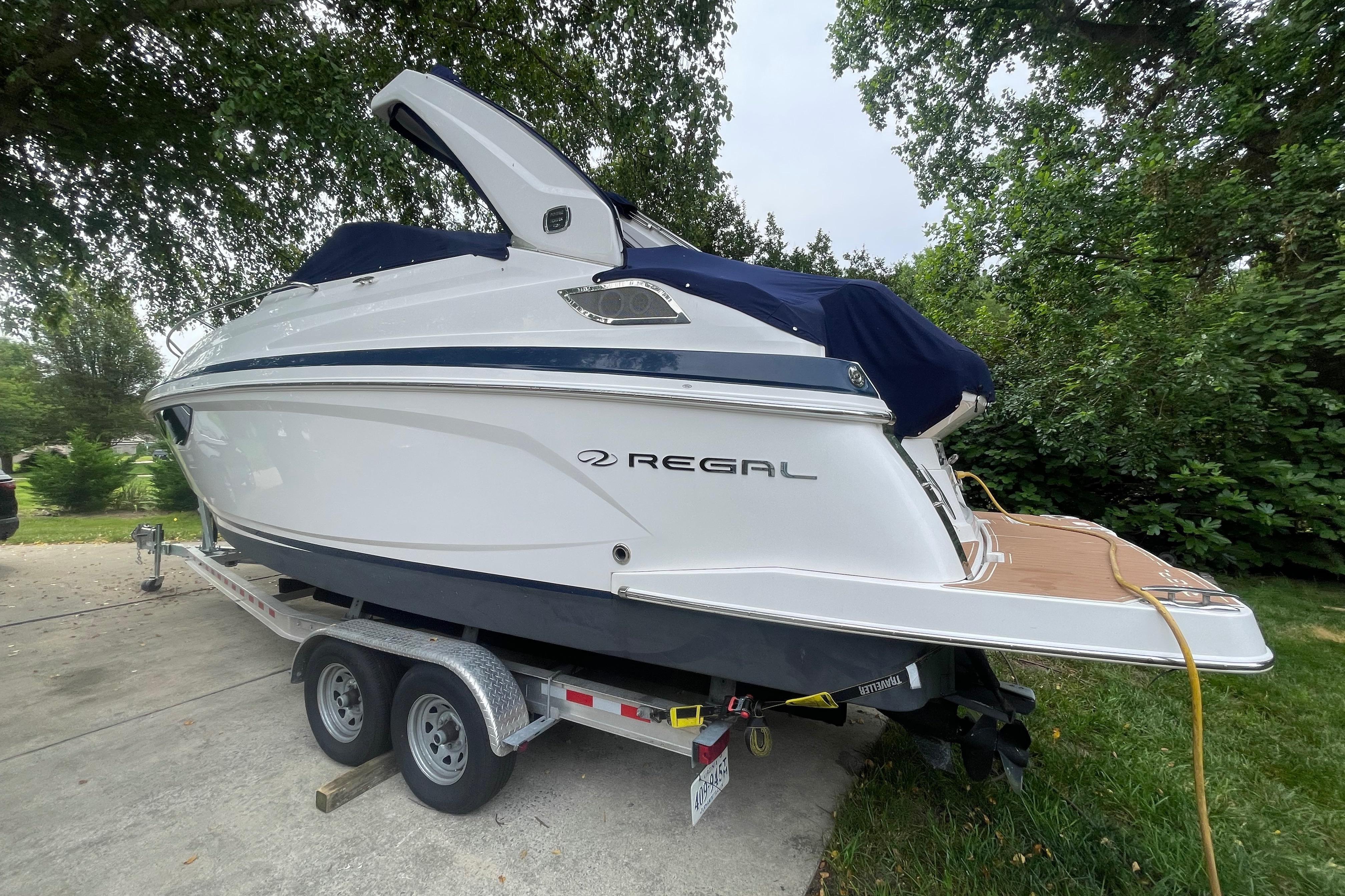 Regal 28 Express 2019 Regal 28 Express boat on trailer, parked outdoors with trees in the background.