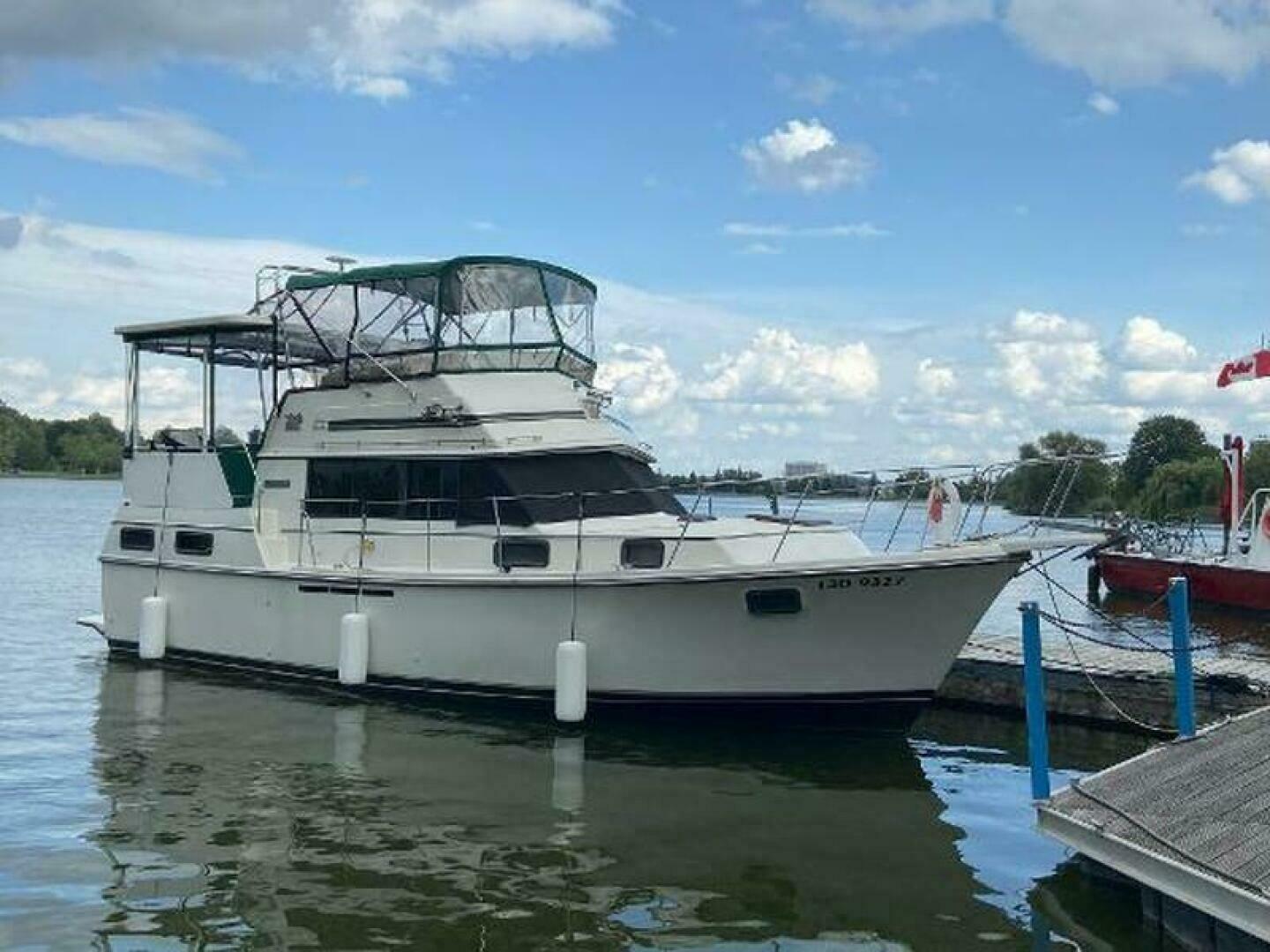 Carver 3607 1987 Carver 3607 yacht docked on a calm lake under a partly cloudy sky.