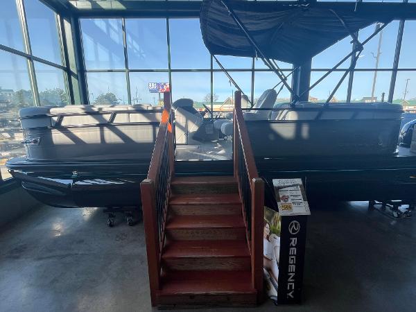 Regency 230 DL3 2025 Regency 230 DL3 pontoon boat displayed indoors with wooden stairs.