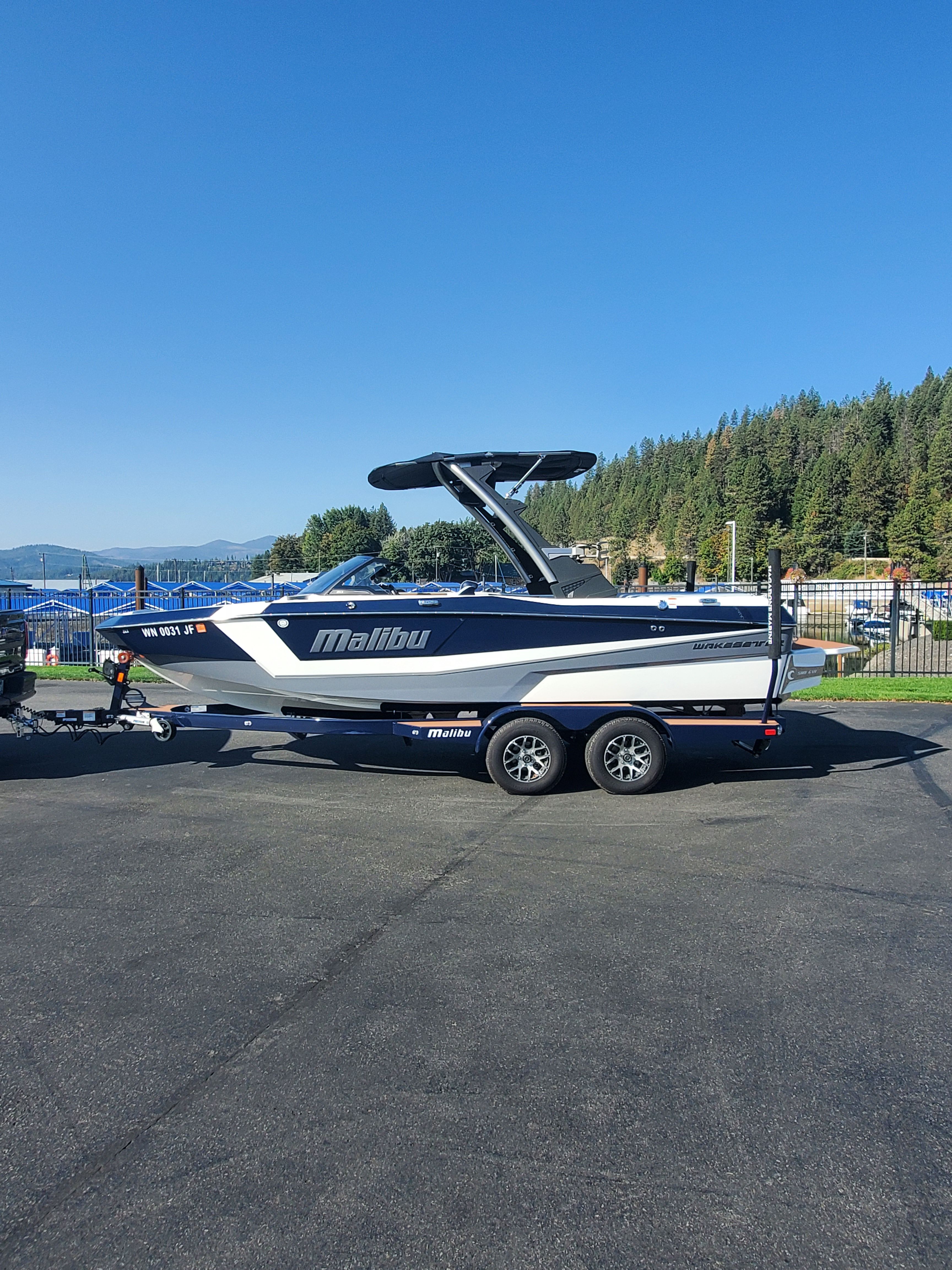 Malibu Wakesetter 21 LX 2023 Malibu Wakesetter 21 LX boat on trailer, parked outdoors under clear blue sky.