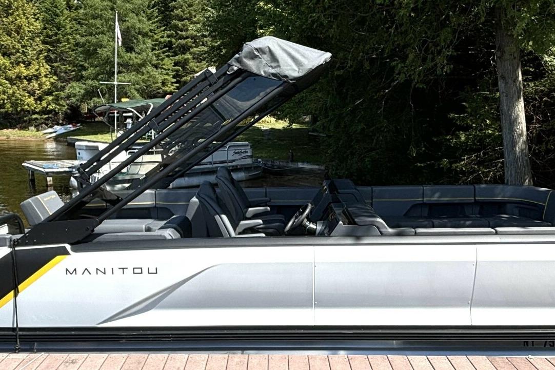 Manitou Explore 24 Navigator 2023 Manitou Explore 24 Navigator pontoon boat docked by a scenic lakeside.