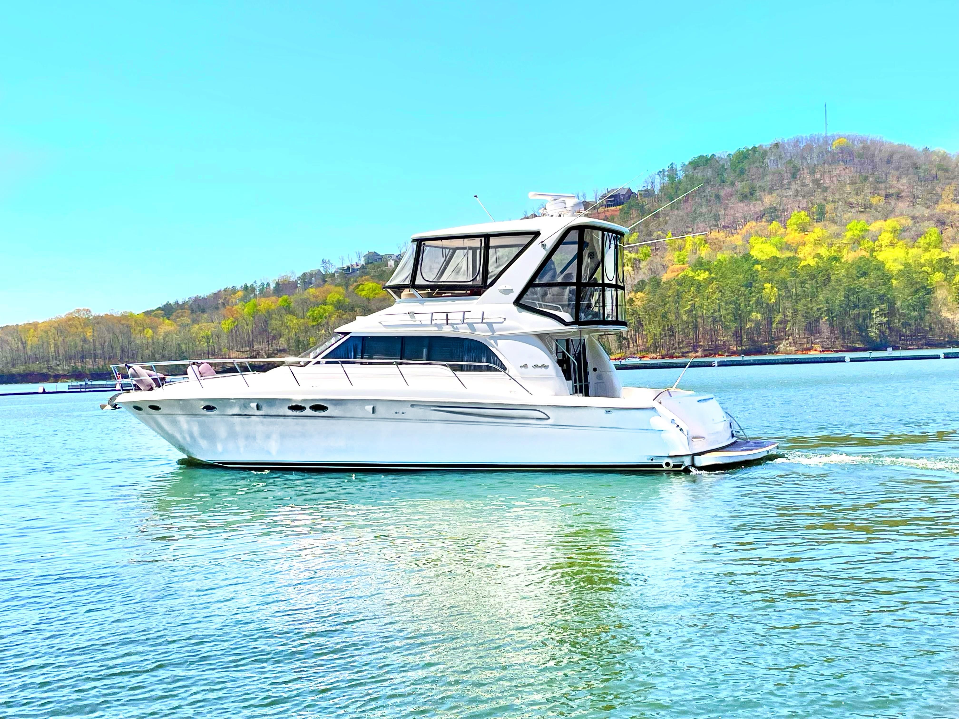 Sea Ray 480 Sedan Bridge 1999 Sea Ray 480 Sedan Bridge yacht cruising on a serene lake with forested hills.