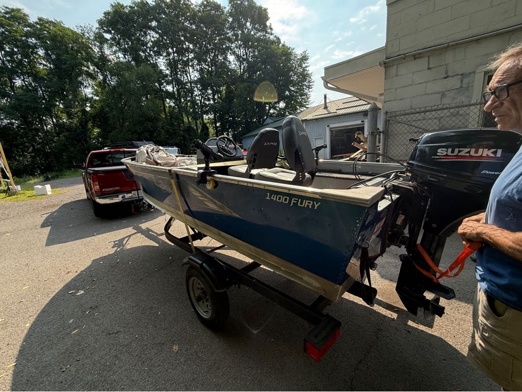 Lund 1400 Fury Tiller 2021 Lund 1400 Fury Tiller boat on trailer, attached to red truck, outdoors.
