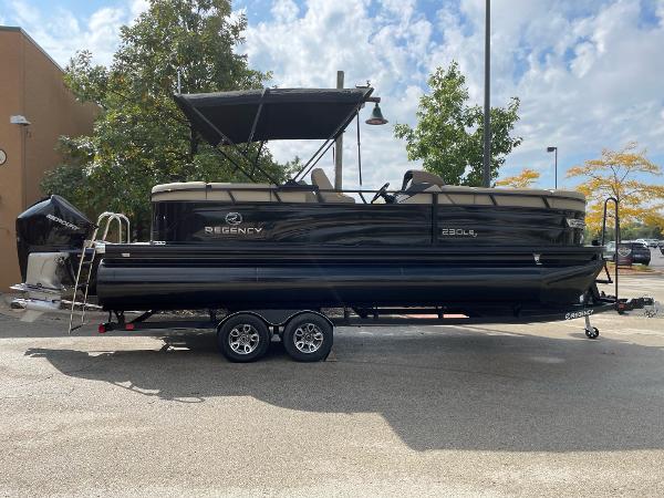 Regency 230 LE3 2023 Regency 230 LE3 pontoon boat on a trailer, black exterior, parked outdoors.