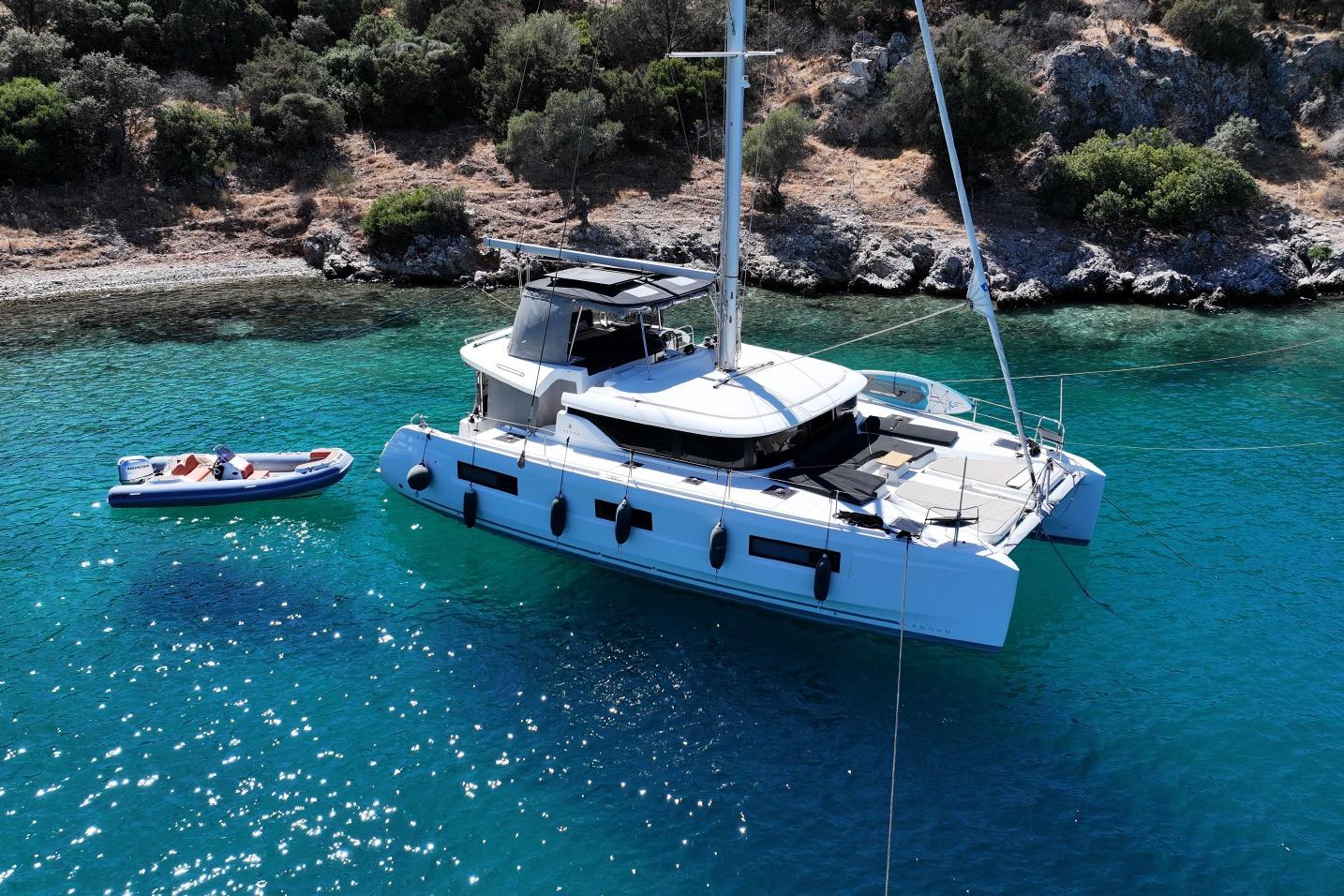 Lagoon 46 2020 Lagoon 46 catamaran anchored in clear turquoise waters near a rocky shoreline.