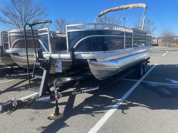 Sun Tracker Fishin' Barge 22 DLX 2025 Sun Tracker Fishin' Barge 22 DLX pontoon boat on trailer in parking lot.