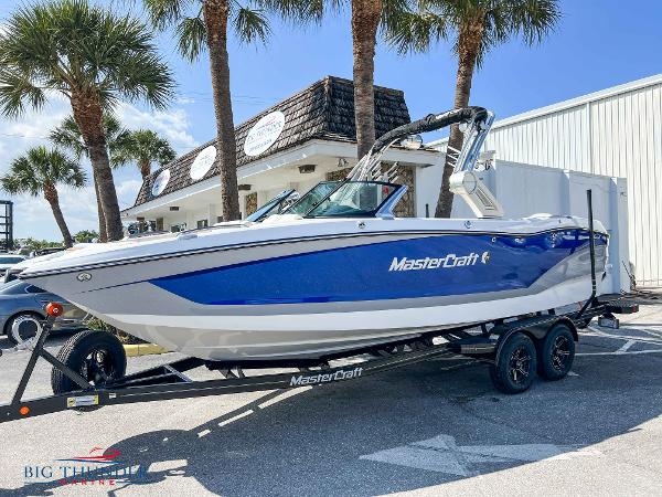 MasterCraft X24 2023 MasterCraft X24 boat on trailer, blue and white, parked near palm trees.